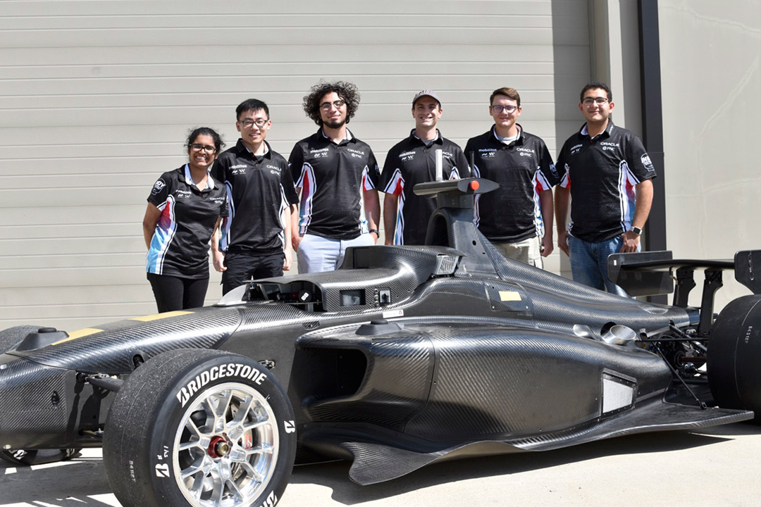 six students pose behind autonomous Indy car.