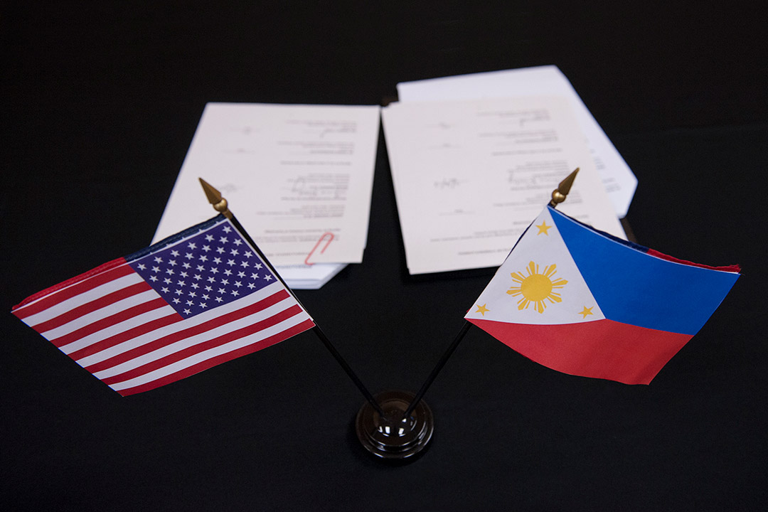 small American and Phillippine flags in the foreground and paperwork in the background.