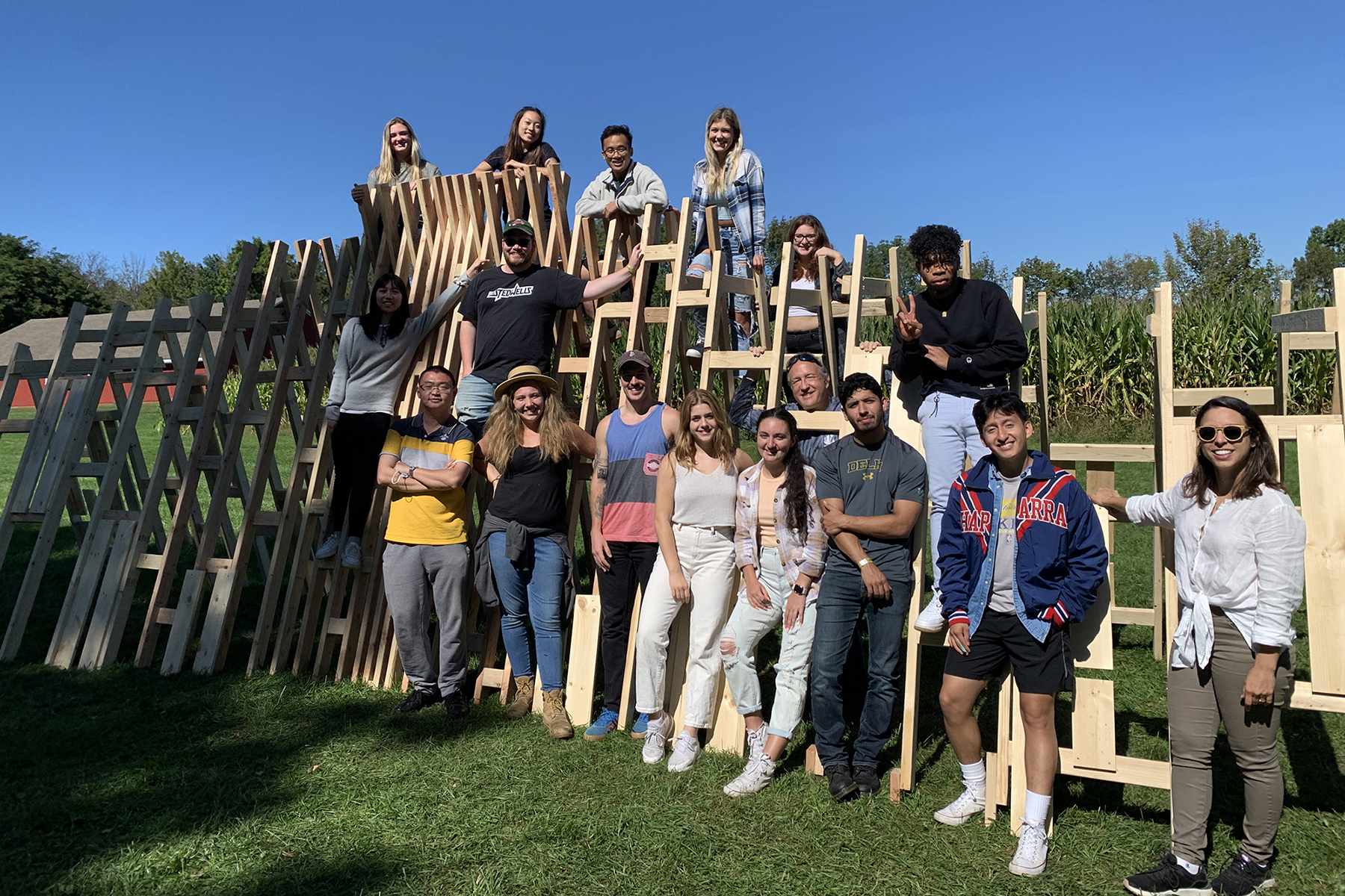 A group of RIT designers and architects post for a photo on the temporary wood installation they created on the grounds of the 1969 Woodstock festival.