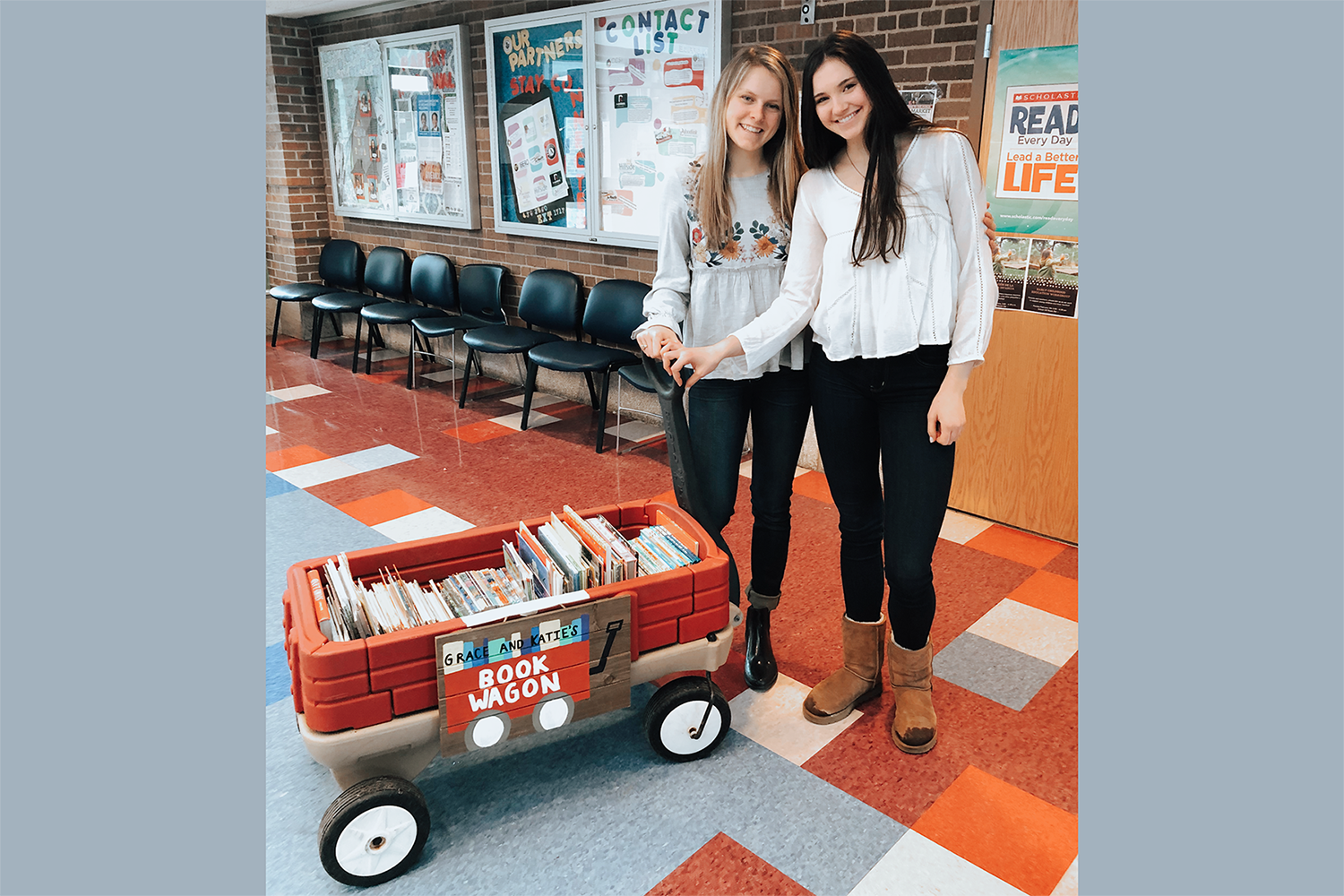 Two girls stand next to a wagon full of books.