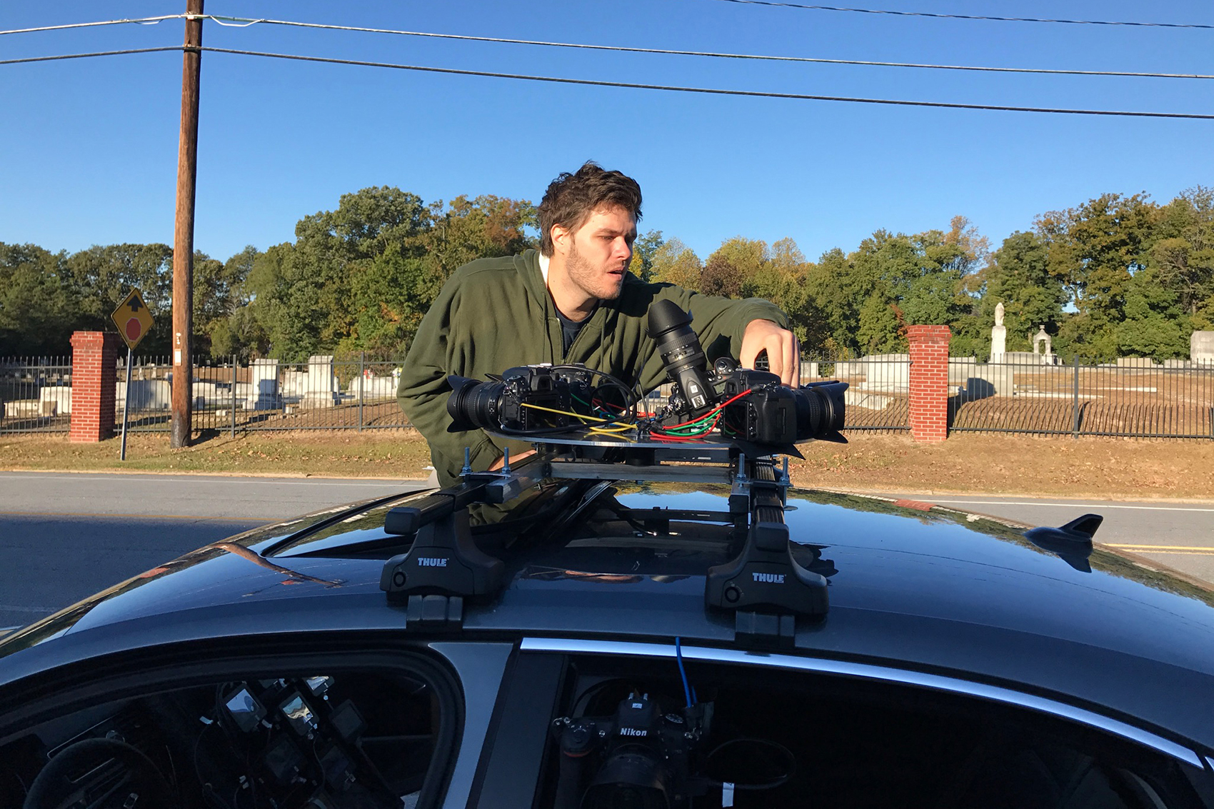 A person operates a camera rig on top of a car.