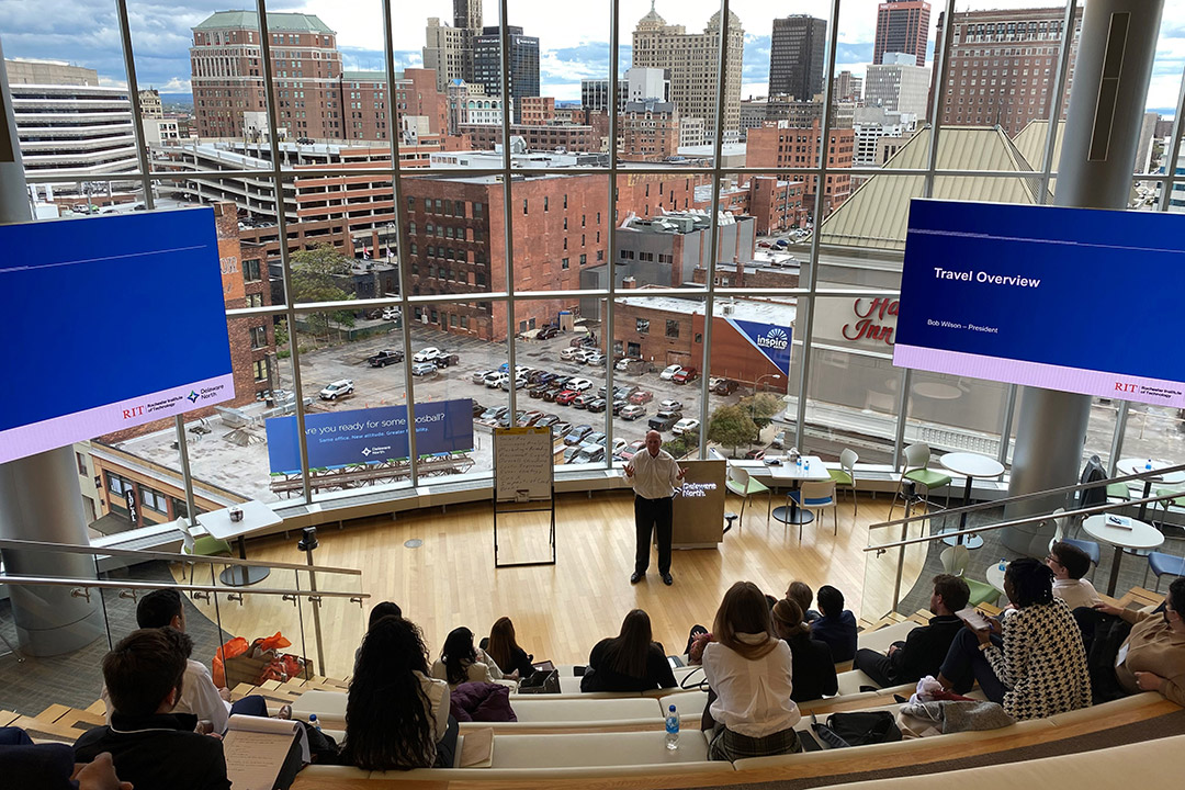 meeting in a large room with a rounded wall of windows facing a city landscape.