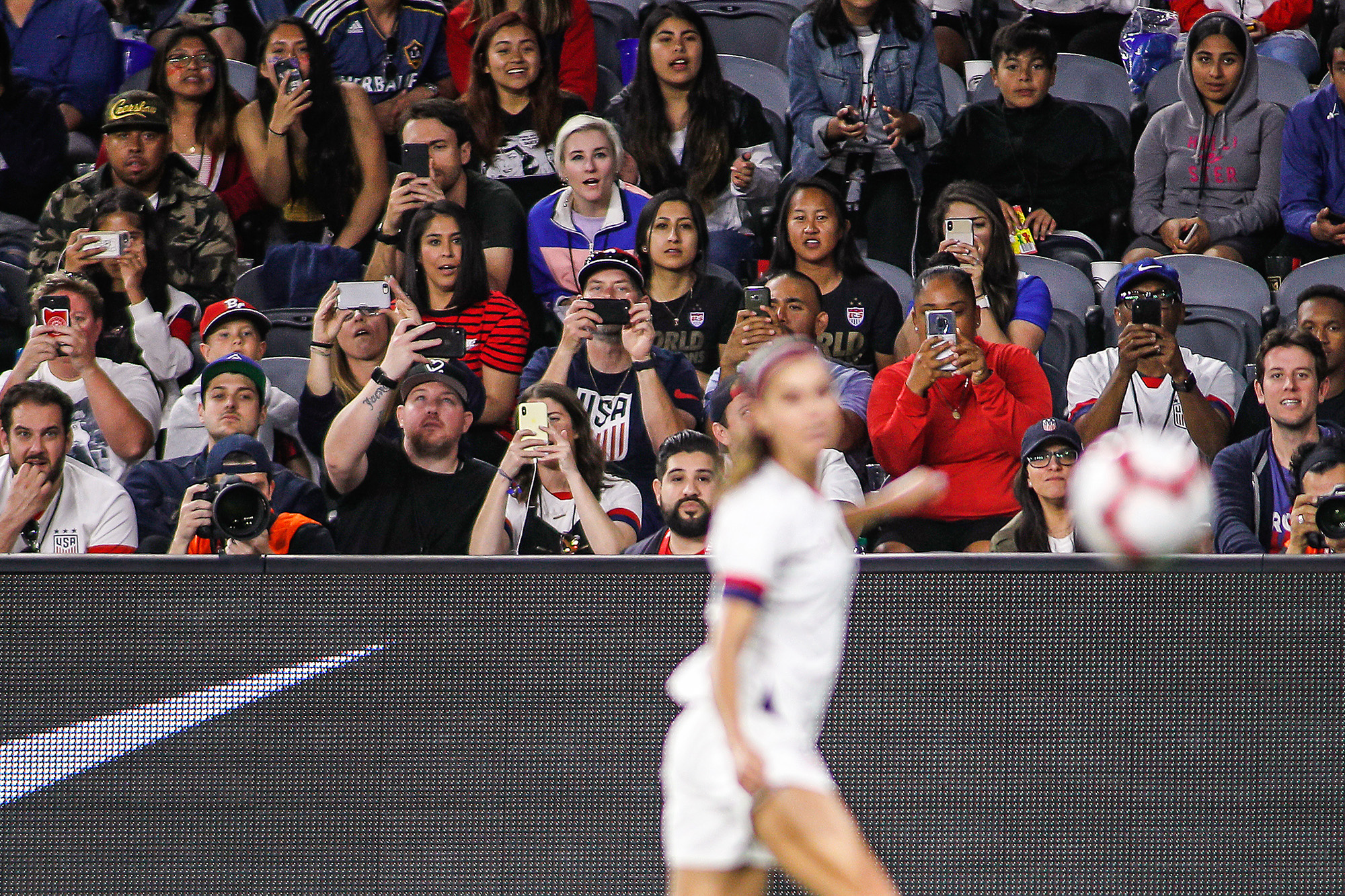 Fans in stands take photographs of soccer star Alex Morgan.