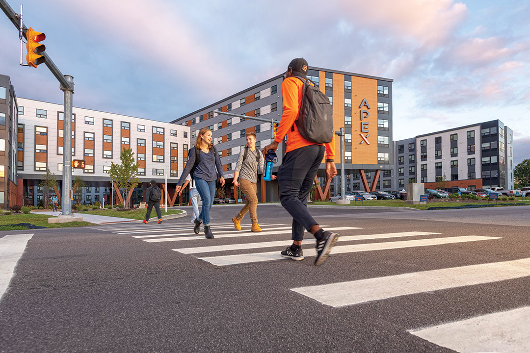 composite photo of people crossing a street in front of a new apartment complex.