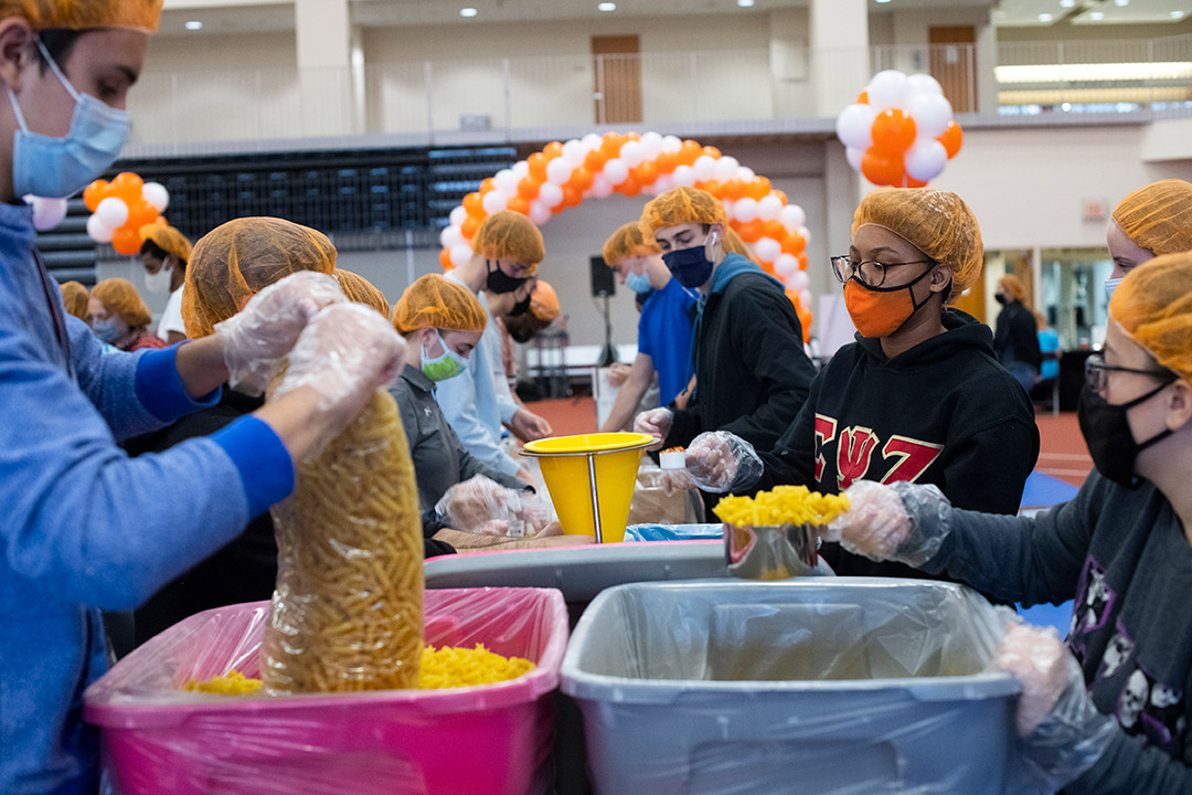 students working in an assembly line to fill bags with ingredients for meals.