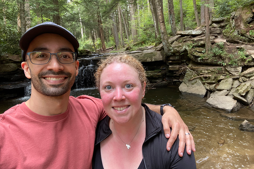 couple posing near a small waterfall in a forested area.