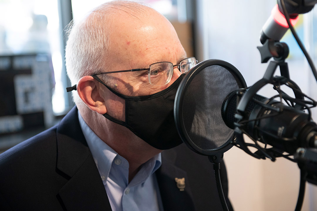 RIT President Munson wearing a mask and speaking into a microphone in a radio station.