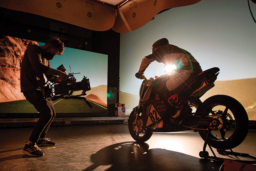 student in a studio filming a person sitting on a motorcycle.