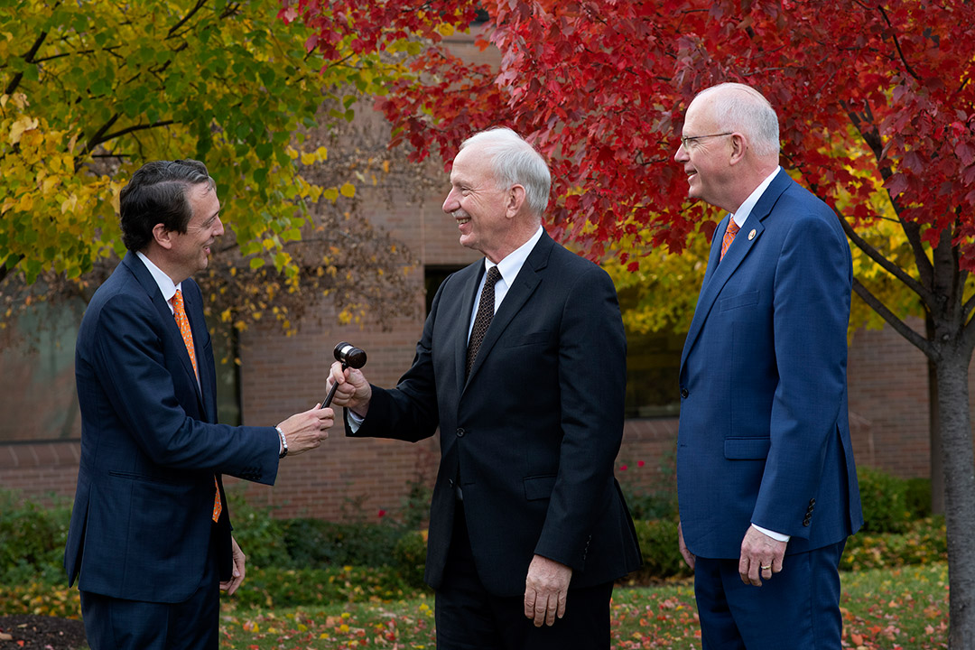 man hands a gavel to another man outdoors.