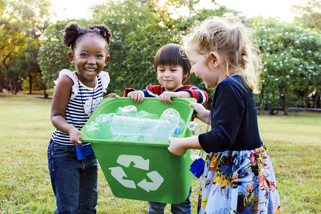 three children holding a recycling bin full of plastic waterbottles.