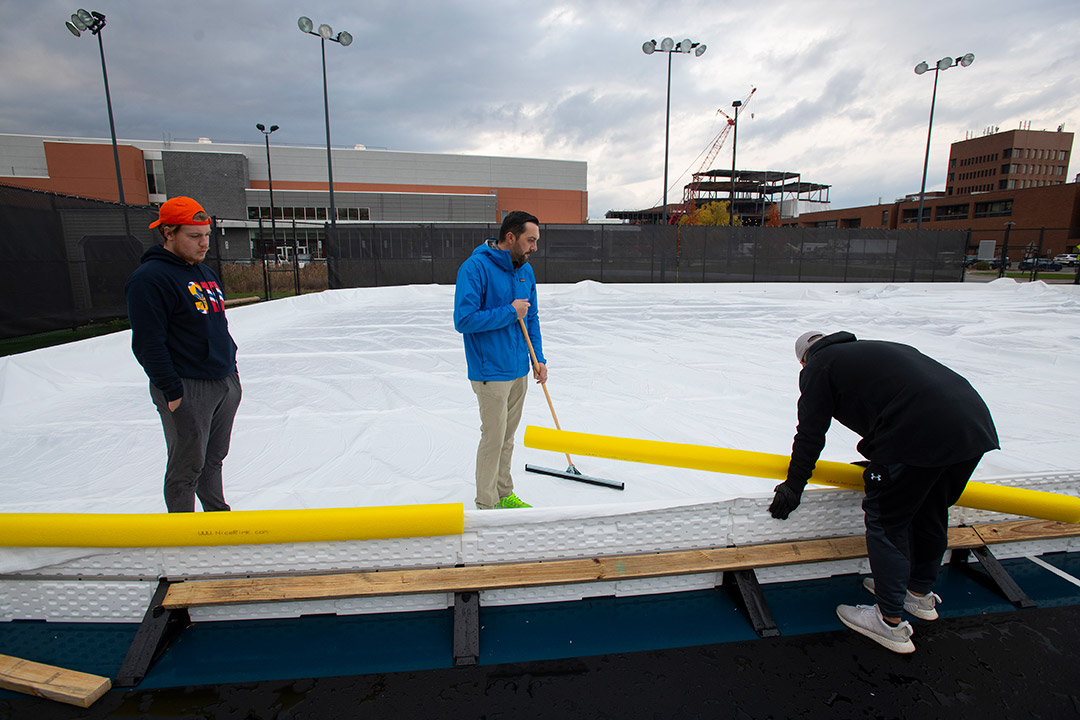 three people working on setting up an outdoor ice rink.