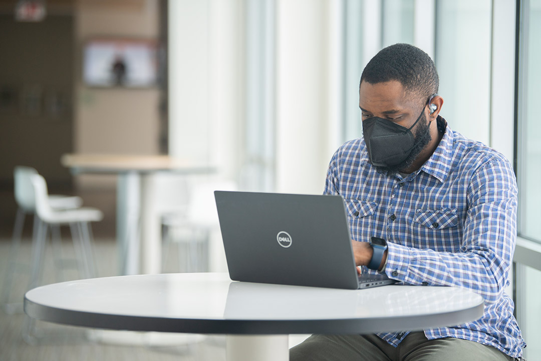 person wearing a hearing aid and a mask working on a laptop.