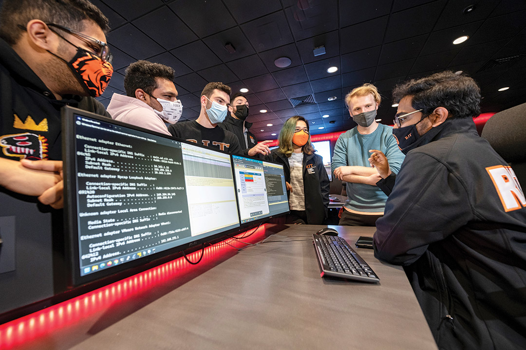 student cybersecurity team huddling around two computer screens.