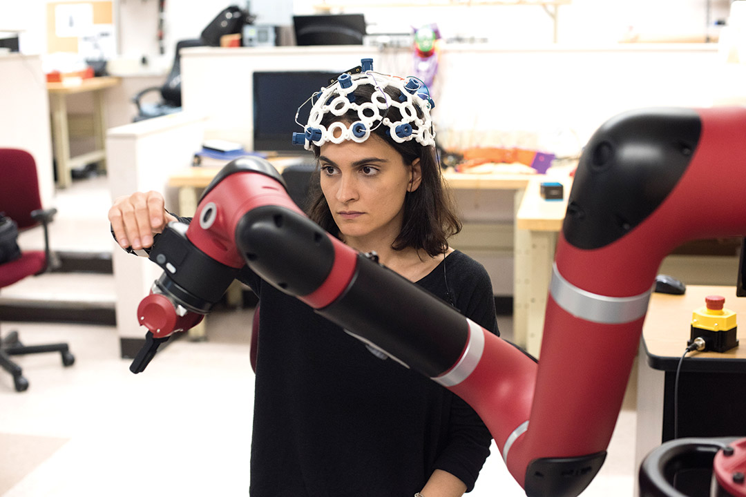 student wearing sensors on her head adjusts a robotic arm.
