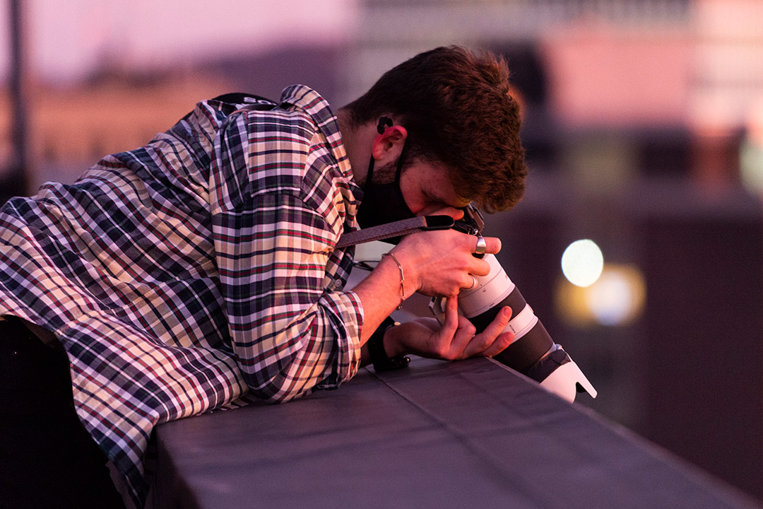 student leaning over a ledge taking a photo with a telescopic lens.