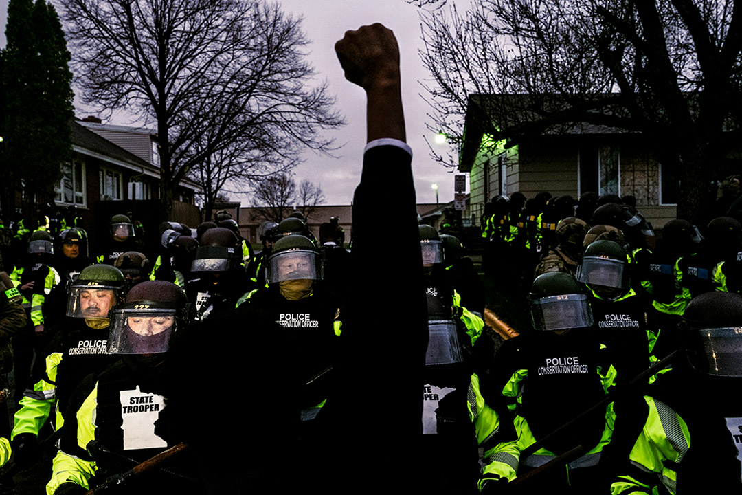 a person raising a fist in the air in front of riot control police officers.
