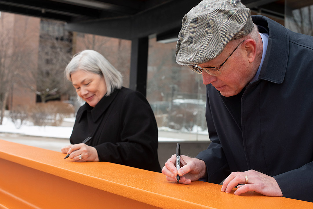 two people signing an orange support beam.