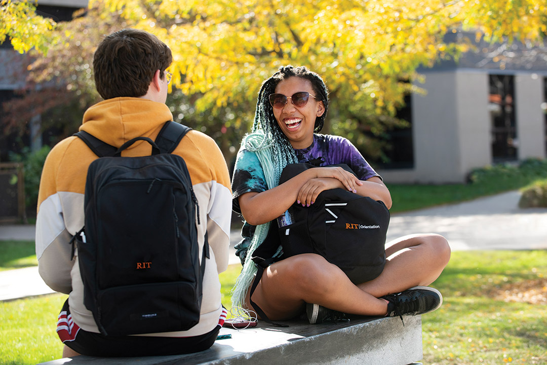 two students sitting outside and laughing.