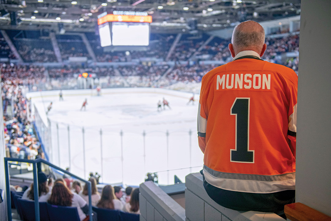 President Munson wearing a No. 1 jersey watches a hockey game in Blue Cross Arena.