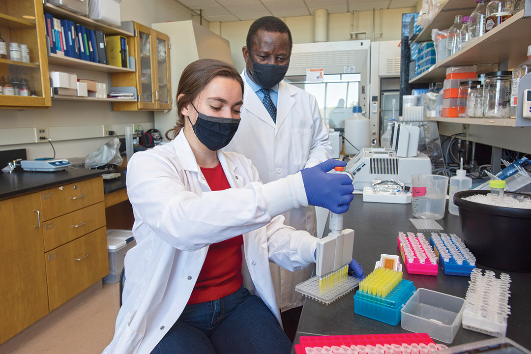 student using pipette as researcher looks on.