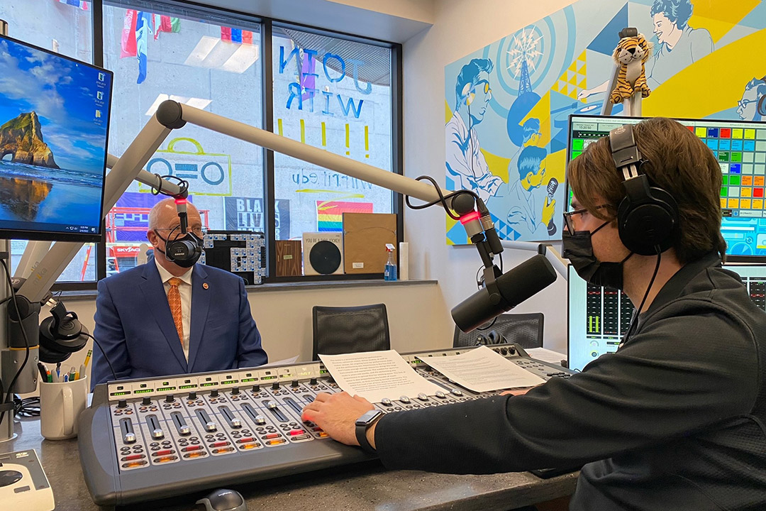 RIT President Munson wearing a mask and speaking into a microphone in a radio station.