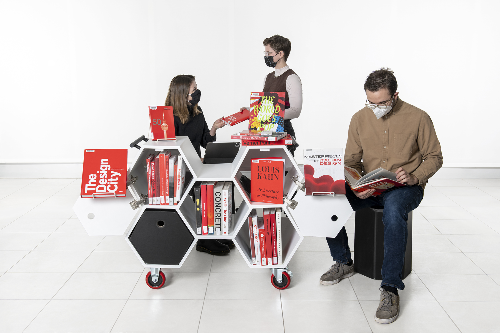 A collection of design books displayed on the Hexacart with students gathering around it.