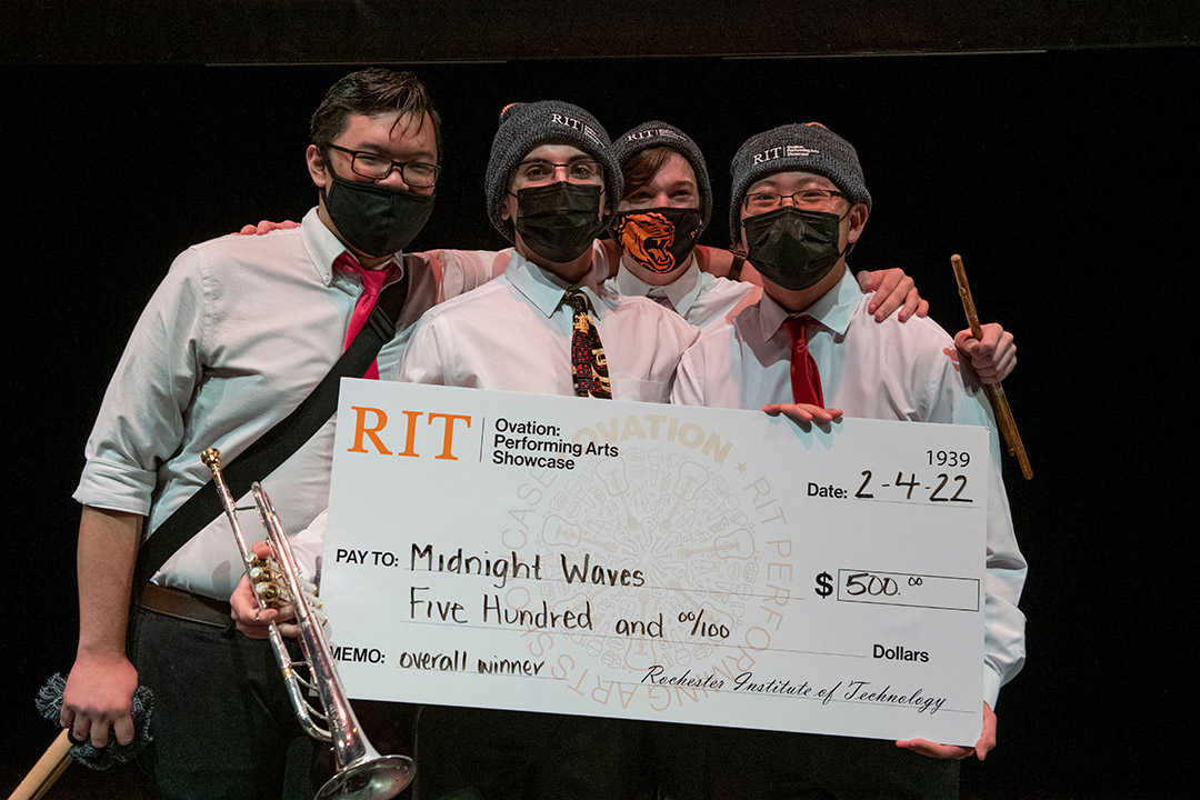 four band members holding a giant novelty check for $500.