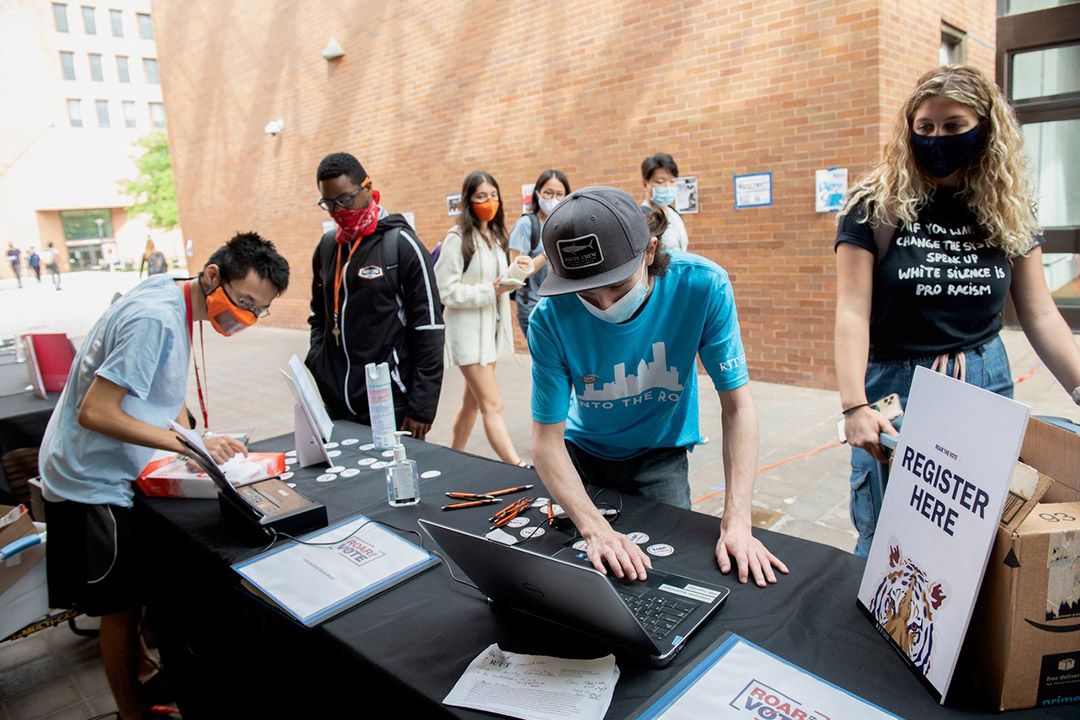 students working at a voting registration table outdoors.