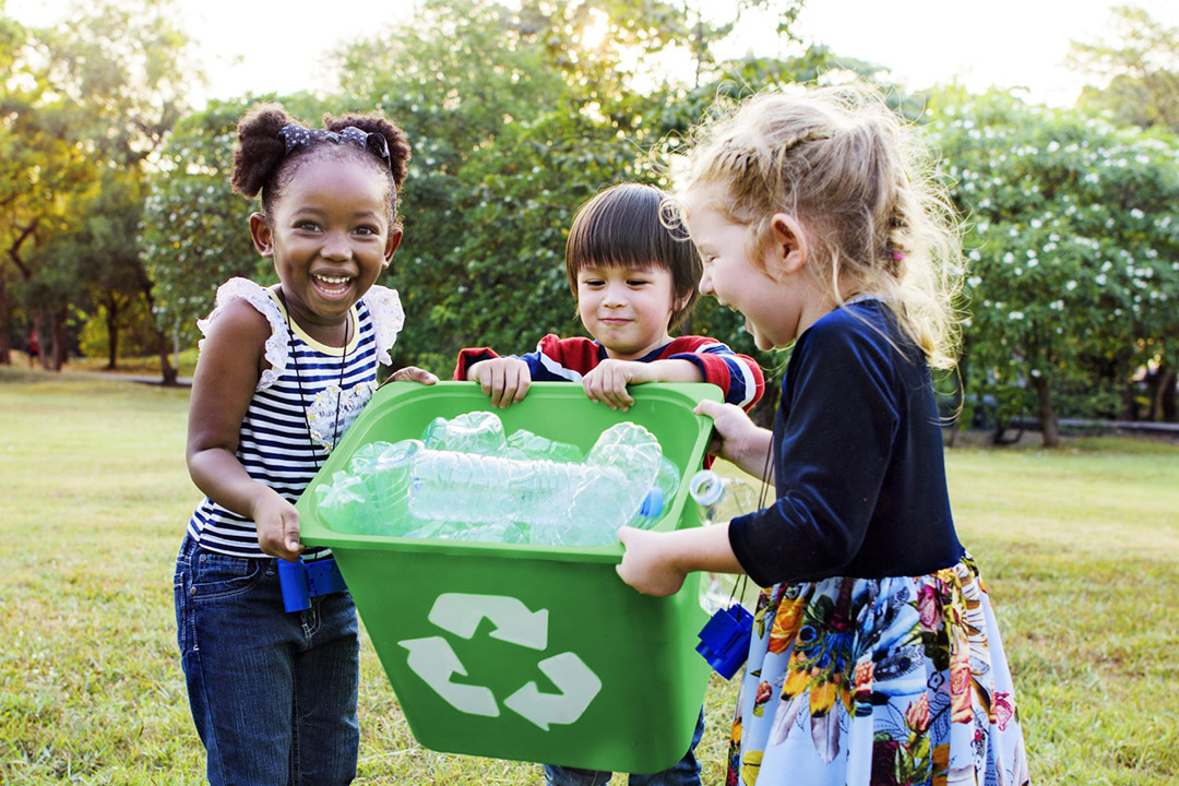 three children holding a recycling bin full of plastic waterbottles.