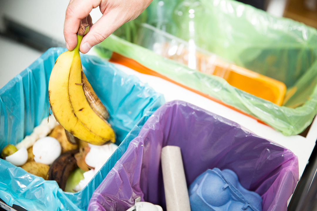 person throwing away a banana peel into a container with other food waste.