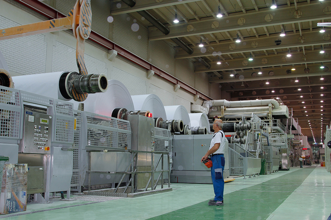 man standing in a factory looking a giant rolls of paper.