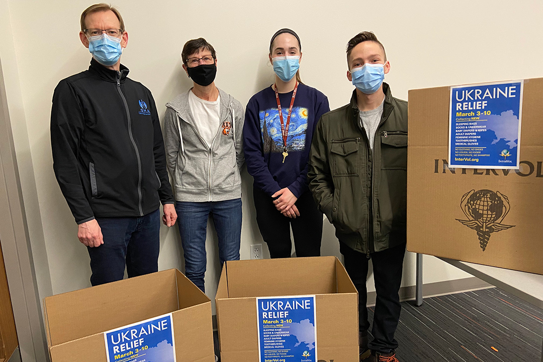 four people wearing masks and standing with cardboard boxes for donations to Ukraine.