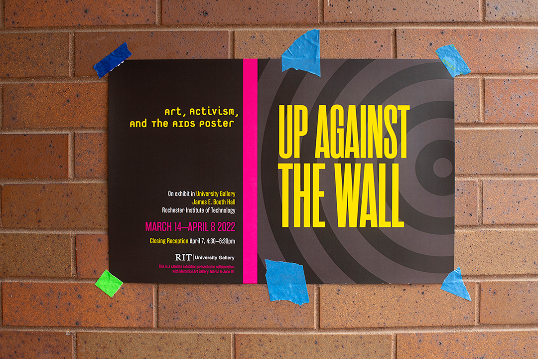 poster for Up Against the Wall exhibit taped to a brick wall.