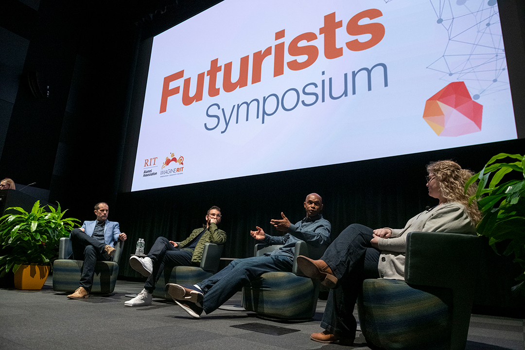 four panelists sit on a stage before a large screen that says, Futurists Symposium.