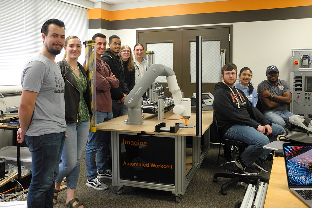 nine students sitting in a lab with a new robotic arm assembly.
