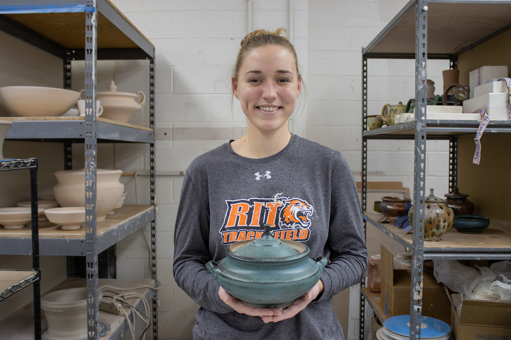 Marian Draper holds one of her vessels in her personal workspace in RIT's ceramics studio.