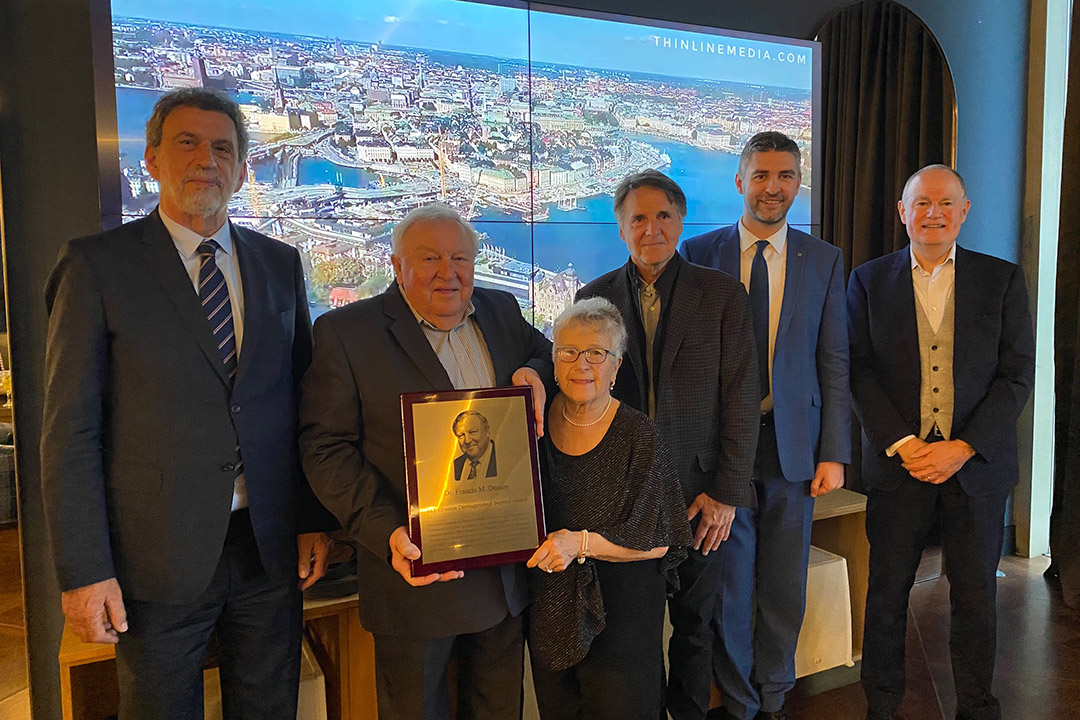 six people posing for a photo as one holds a commemorative plaque.