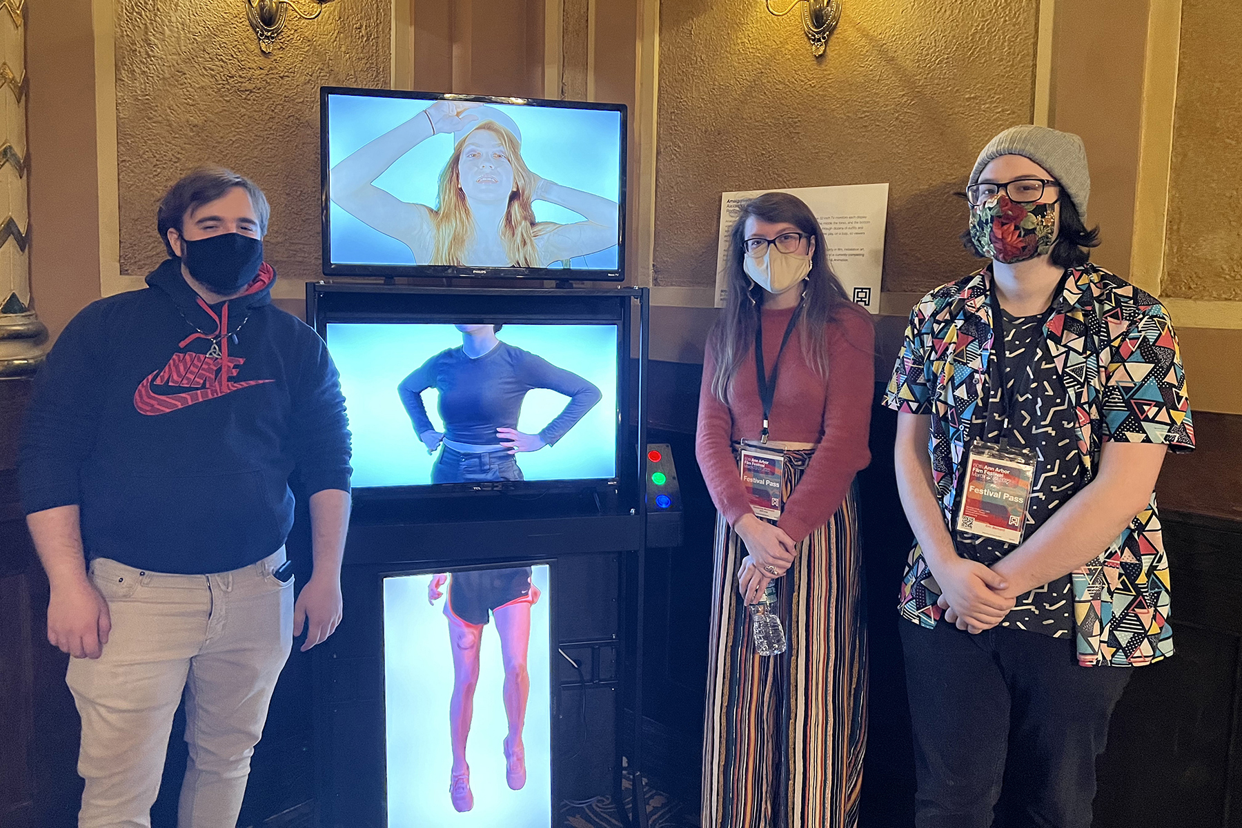 Three people stand around Amalgamate, a three-channel video display.