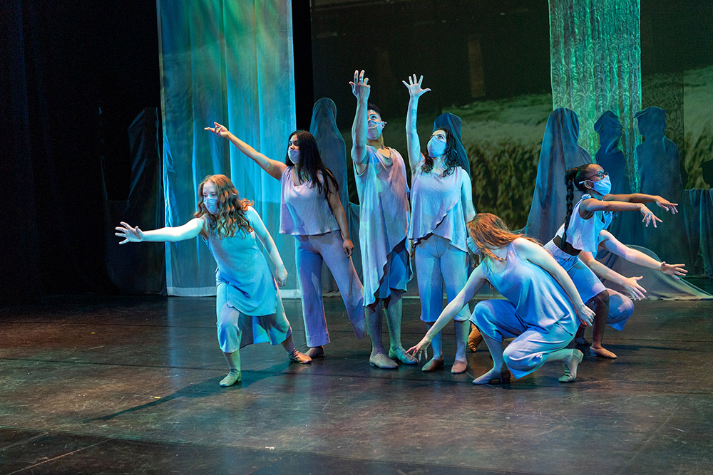 seven dancers dressed in shades of blue and purple reaching out in various directions.