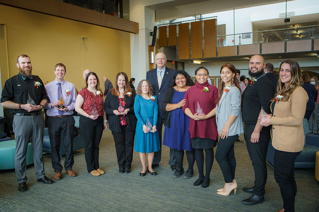 group of people standing in a semi-circle holding glass awards.