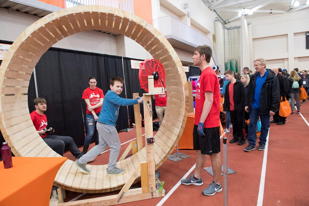 a child walking in a person-sized wooden hamster wheel.