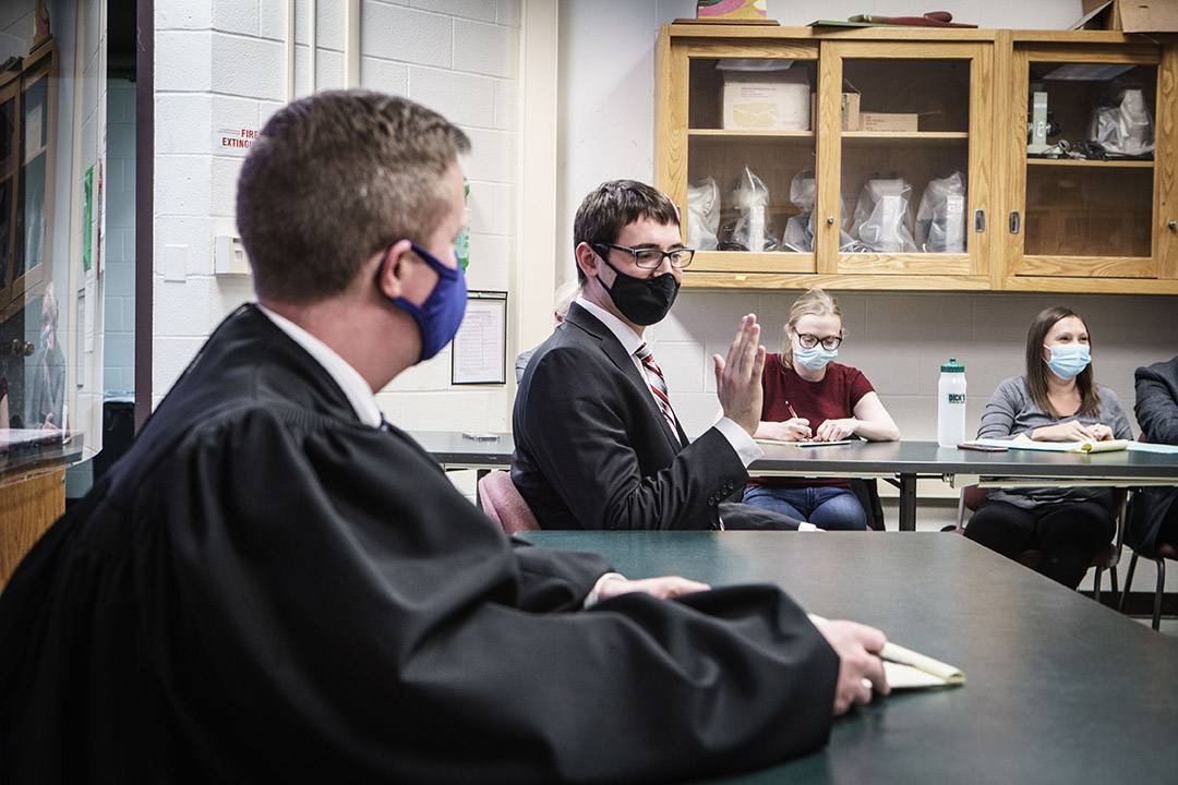 student holding up his hand as if taking an oath in a mock trial.