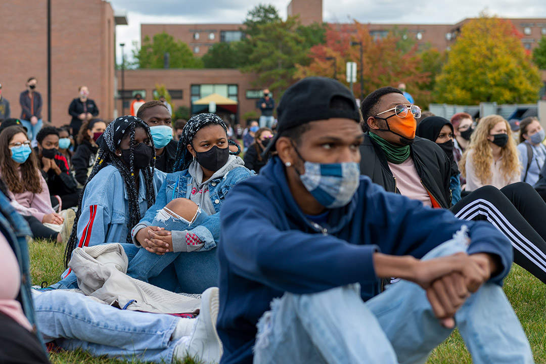 group of students wearing face masks sitting on a lawn.