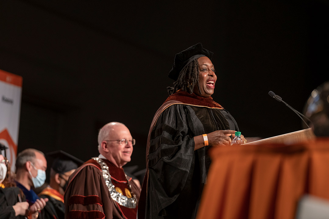 woman wearing commencement regalia speaking at a podium.