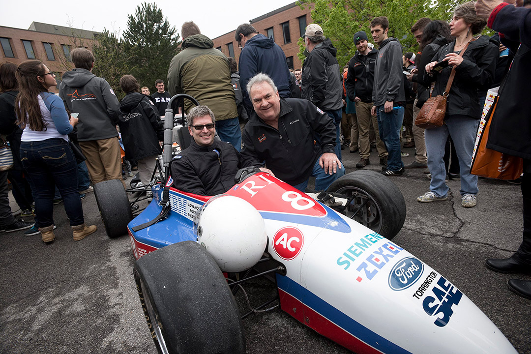 person sitting in a Formula racecar and another person crouching down next to the car.