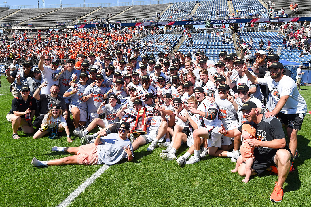entire men's lacrosse seat gathered on the field with a championship trophy.