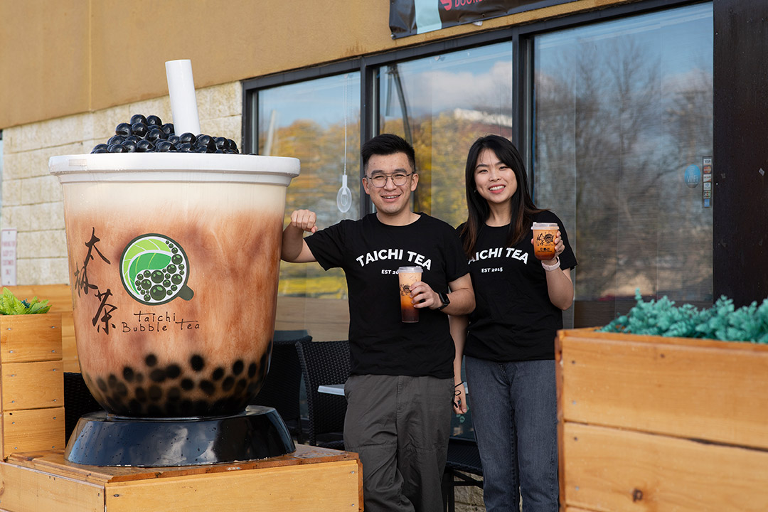 two people holding cups of bubble tea standing outside of the Taichi Bubble Tea store.