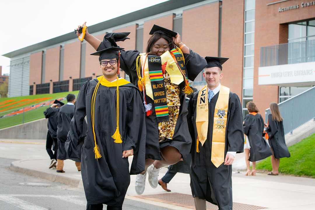 three graduating students wearing their cap and gown and important sashes.