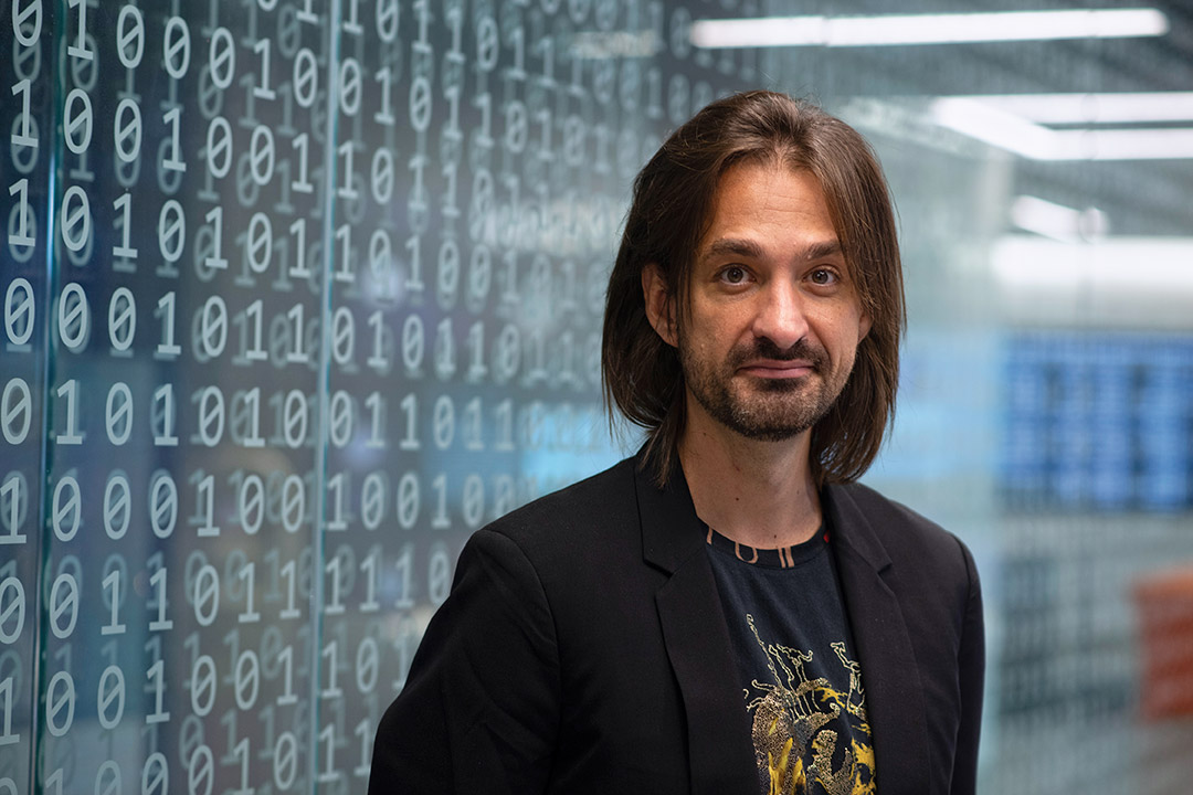 inventor standing in front of a glass wall etched with ones and zeros.