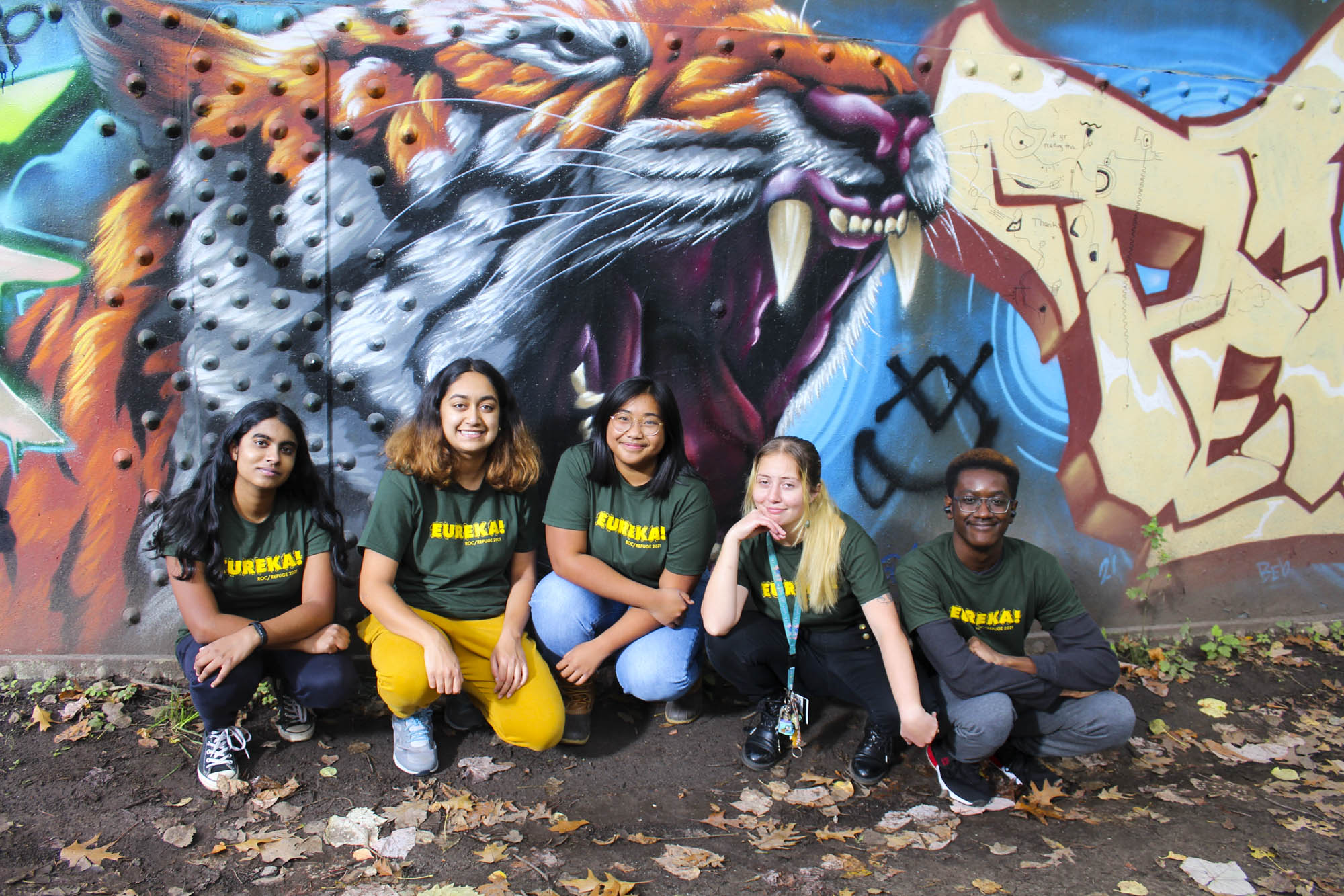 A group of students pose in front of a mural.